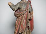 une statue en bois représentant un homme vêtu d'une robe rouge et d'une cape rouge