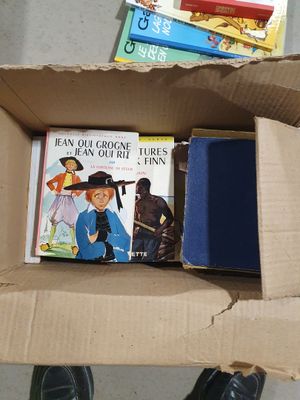 une boîte remplie de livres et une paire de chaussures par terre