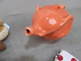 an orange pig shaped teapot sitting on a table next to a bagel