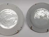 pair of white porcelain plates with silver rims on a white surface
