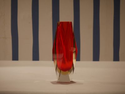 a red vase sitting on a table with a striped wall behind it