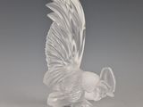 une figurine en verre représentant un oiseau, posée sur un socle transparent