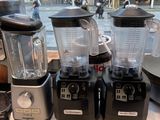 several blenders are lined up on a counter in front of a window