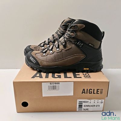 Des chaussures de randonnée pour homme sont posées sur une boîte, sur une surface blanche.