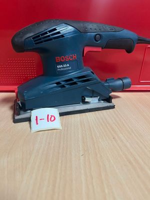 une ponceuse orbitale Bosch posée sur une table à côté d'une boîte rouge