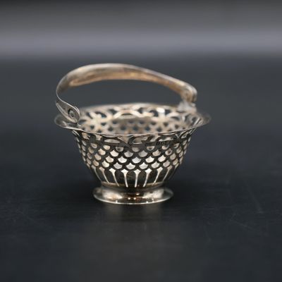 a small silver basket with a handle on a black surface
