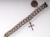 silver chain bracelet with a cross and a coin on a white surface