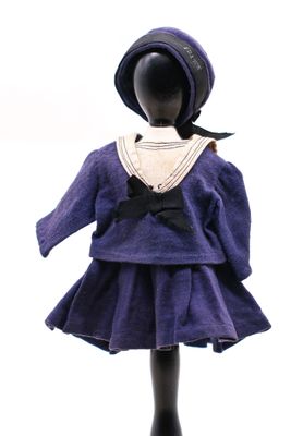 poupée vêtue d'une robe violette et d'un chapeau, posée sur un socle noir