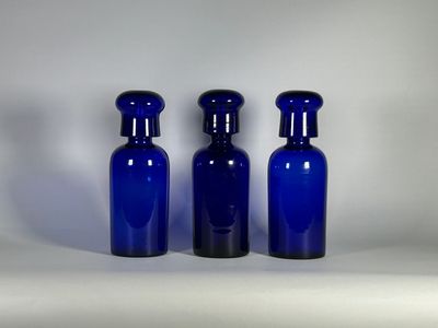 trois bouteilles en verre bleues sont alignées sur une surface blanche