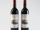 two bottles of red wine sitting next to each other on a white surface