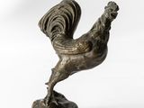 statue en bronze représentant un coq, posée sur un socle en bois, sur fond blanc