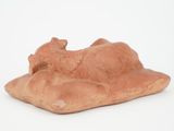 clay figurine of a dog laying on a pillow on a white surface