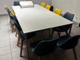 des chaises aux couleurs vives disposées autour d'une table blanche dans une pièce où se trouve un tableau blanc accroché au mur