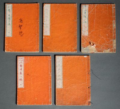quatre livres orange portant des inscriptions en chinois, posés sur une table