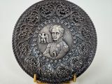 a silver plate with a picture of a woman holding a bird