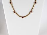 a gold necklace with garnets and pearls on a mannequin