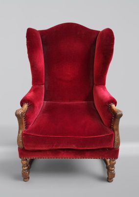 un fauteuil à oreilles en velours rouge, avec des pieds et des accoudoirs en bois