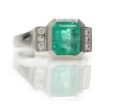 an emerald and diamond ring on a reflective surface