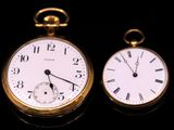 two gold pocket watches sitting side by side on a black surface