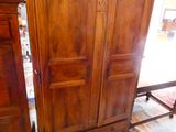 a wooden armoire with a door and a chair in front of it