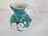 a green vase with flowers on it sitting on a white surface