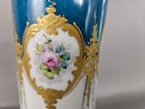 a blue vase with a gold border and a pink rose on it