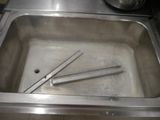 stainless steel sink with two tongs in it and a pot in the background