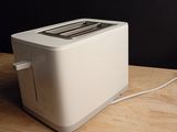 a white toaster on a wooden table with a black wall behind it