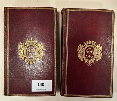 two books with gold and red covers on them sitting on a table