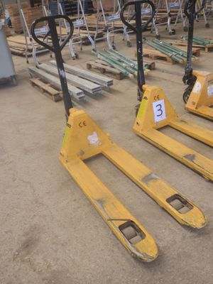 Trois chariots élévateurs jaunes sont garés dans un entrepôt, avec des palettes en arrière-plan.