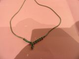 necklace with green beads on a pink surface with a shadow on the ground