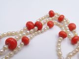 a red and white necklace with pearls on a white surface