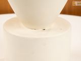 a white vase with a flower in it on a white pedestal