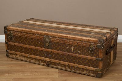 Une malle Louis Vuitton posée sur un parquet, avec un mur en arrière-plan