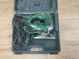 un outil vert et noir dans un étui posé sur un plancher en bois