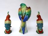 three figurines of parrots sitting on a white surface