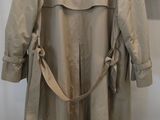 beige trench coat on a hanger in front of a white wall