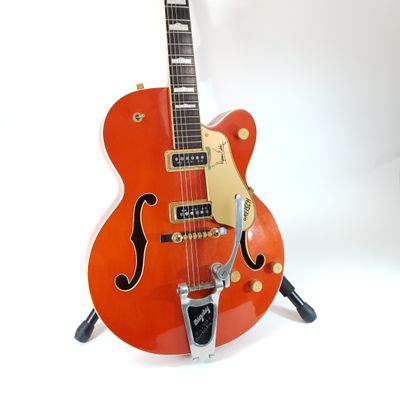 an orange electric guitar sitting on top of a stand on a white surface