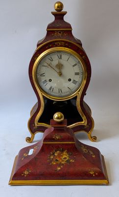 a red and gold clock on a stand on a white background