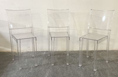 three clear plastic chairs sitting next to each other against a white wall