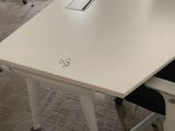 une table blanche sur laquelle est posé un ordinateur portable, dans une pièce