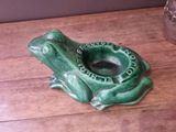 a green frog shaped ashtray on a wooden table