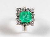 a close up of a green emerald and diamond ring on a white surface