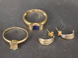trois bagues en or et une bague ornée d'une pierre bleue sur un fond noir
