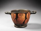 un vieux vase noir et orange sur lequel est représenté un hibou, sur le côté