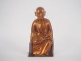 statue of a monk sitting on a stool with a white background
