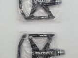 two black pedals in plastic bags on a white surface
