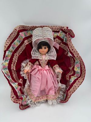 poupée en robe rose et avec un bonnet, assise sur une couverture rouge