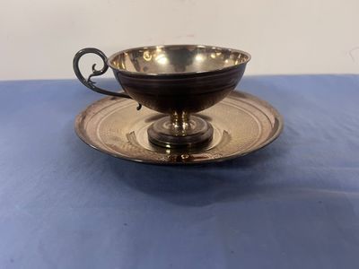 une tasse et une soucoupe plaquées argent posées sur une nappe bleue