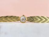 une montre-bracelet en or avec un cadran blanc posée sur une surface en marbre